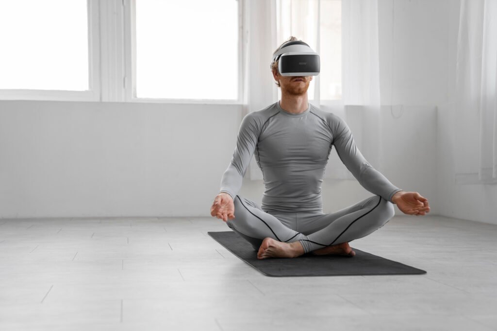 Man wearing virtual reality headset sits cross-legged on yoga mat indoors, practicing meditation with technology-enhanced mindfulness experience.